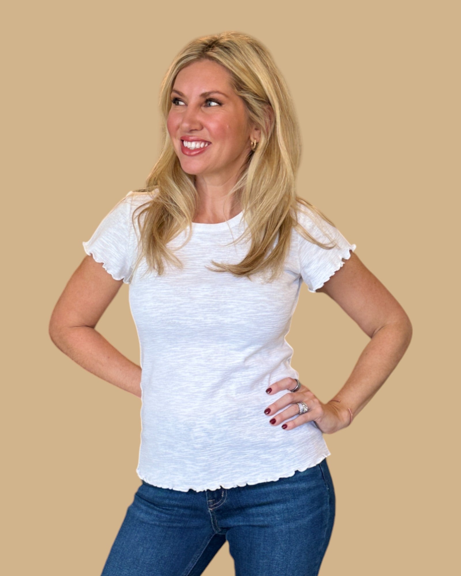 Woman wearing a white short-sleeve tee with ruffled edges, paired with dark wash skinny jeans. Casual, fitted white t-shirt for women, perfect for everyday wear. Available at Wish Upon Boutique.