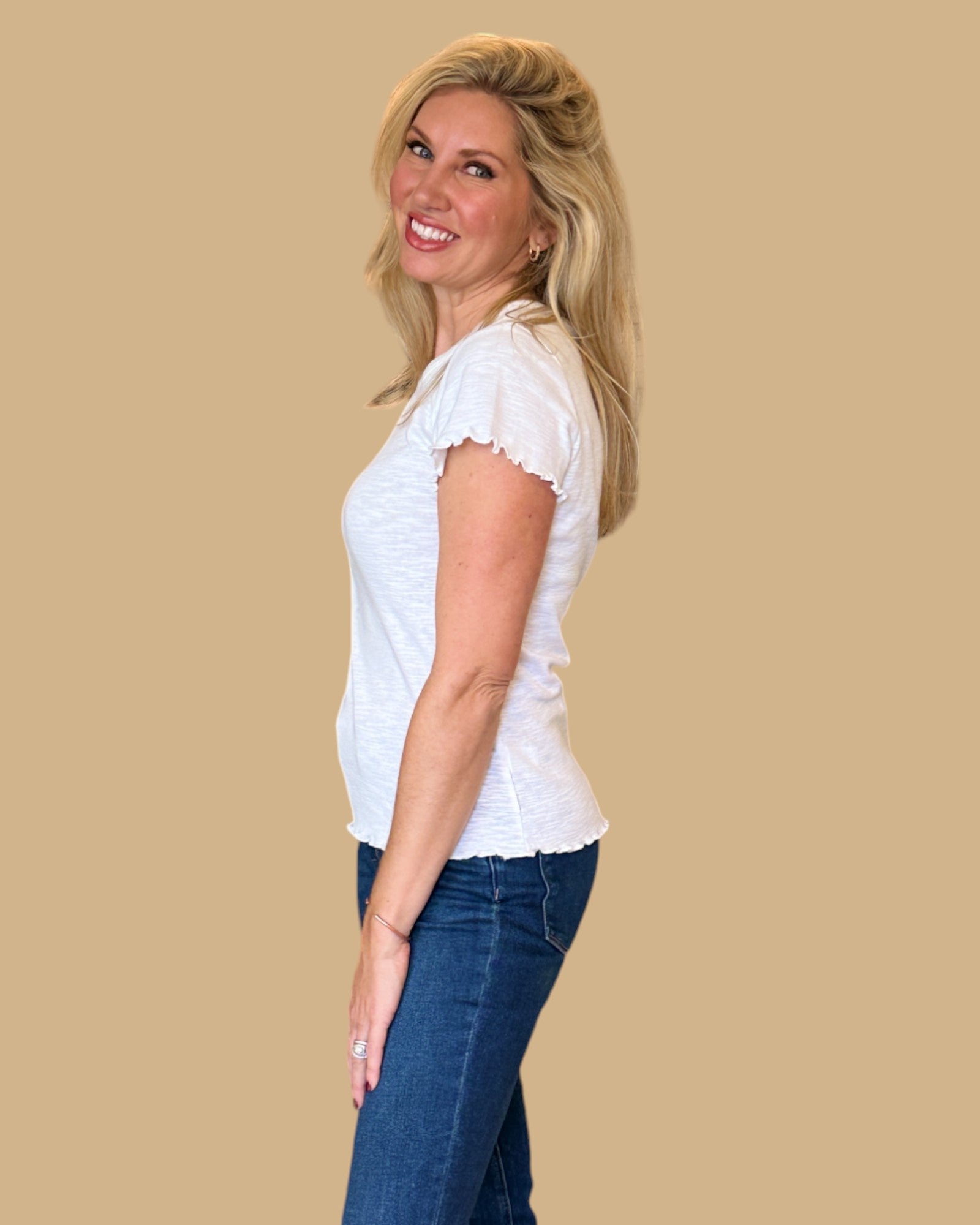 Woman wearing a white short-sleeve tee with ruffled edges, paired with dark wash skinny jeans. Casual, fitted white t-shirt for women, perfect for everyday wear. Available at Wish Upon Boutique.