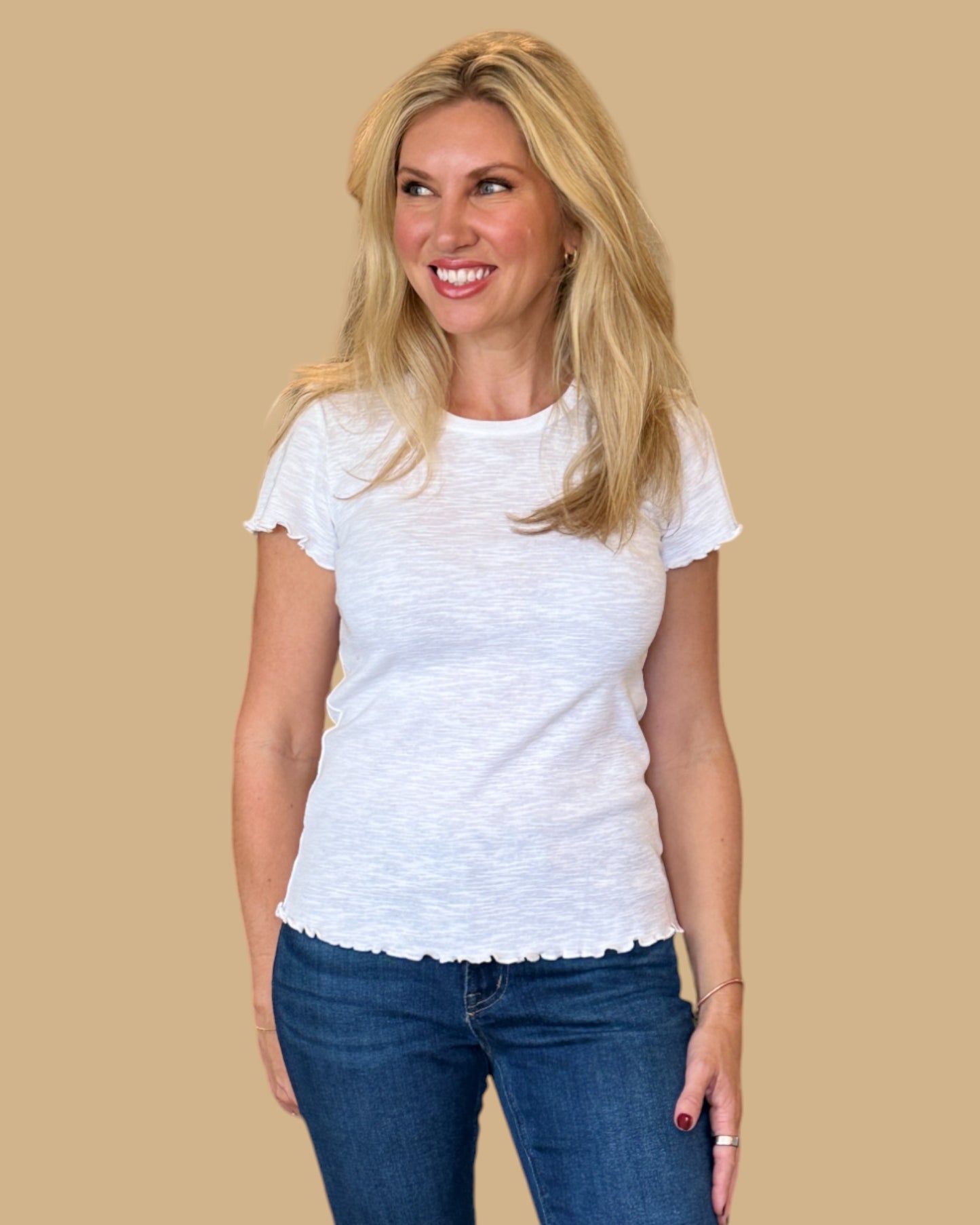 Woman wearing a white short-sleeve tee with ruffled edges, paired with dark wash skinny jeans. Casual, fitted white t-shirt for women, perfect for everyday wear. Available at Wish Upon Boutique.