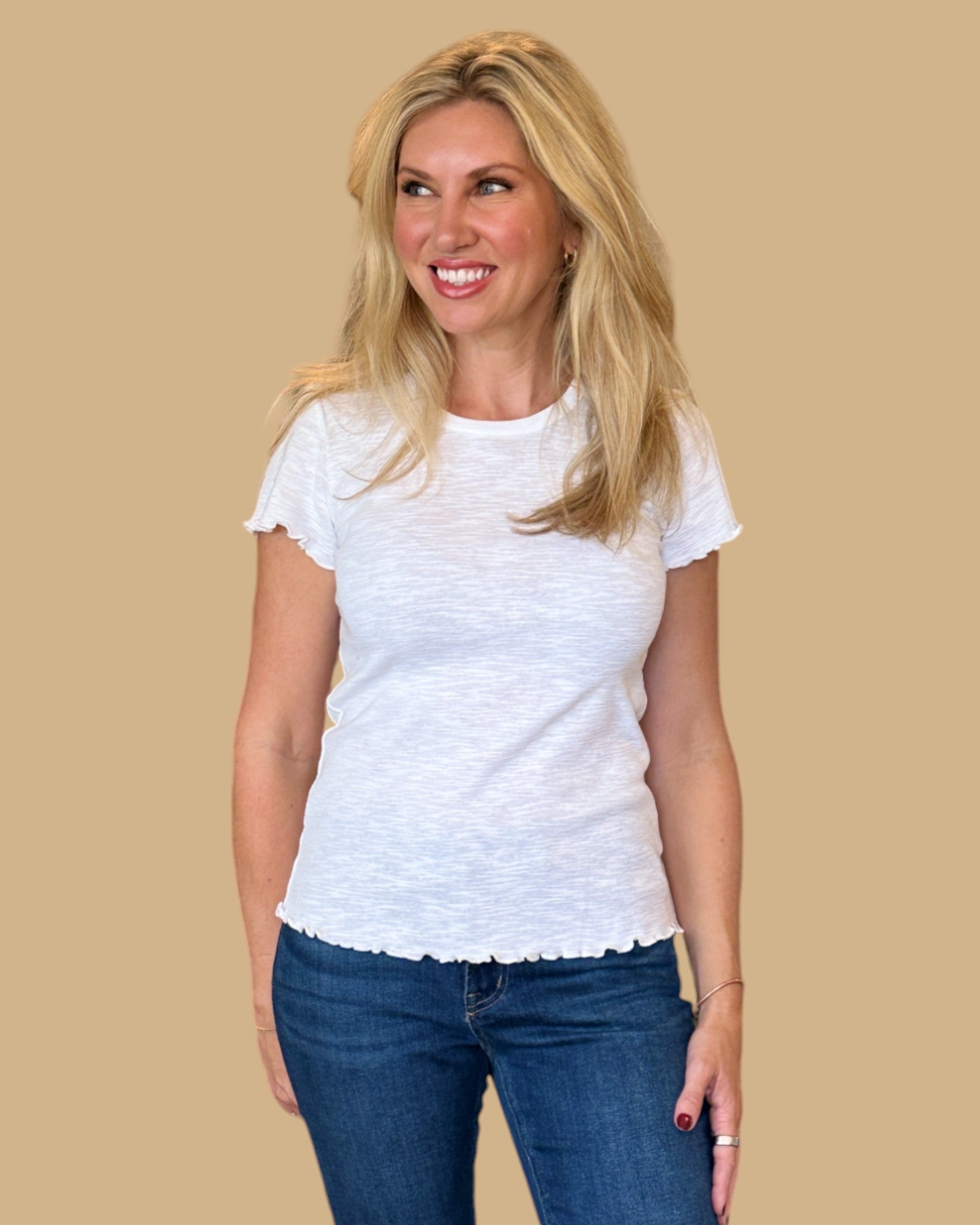 Woman wearing a white short-sleeve tee with ruffled edges, paired with dark wash skinny jeans. Casual, fitted white t-shirt for women, perfect for everyday wear. Available at Wish Upon Boutique.