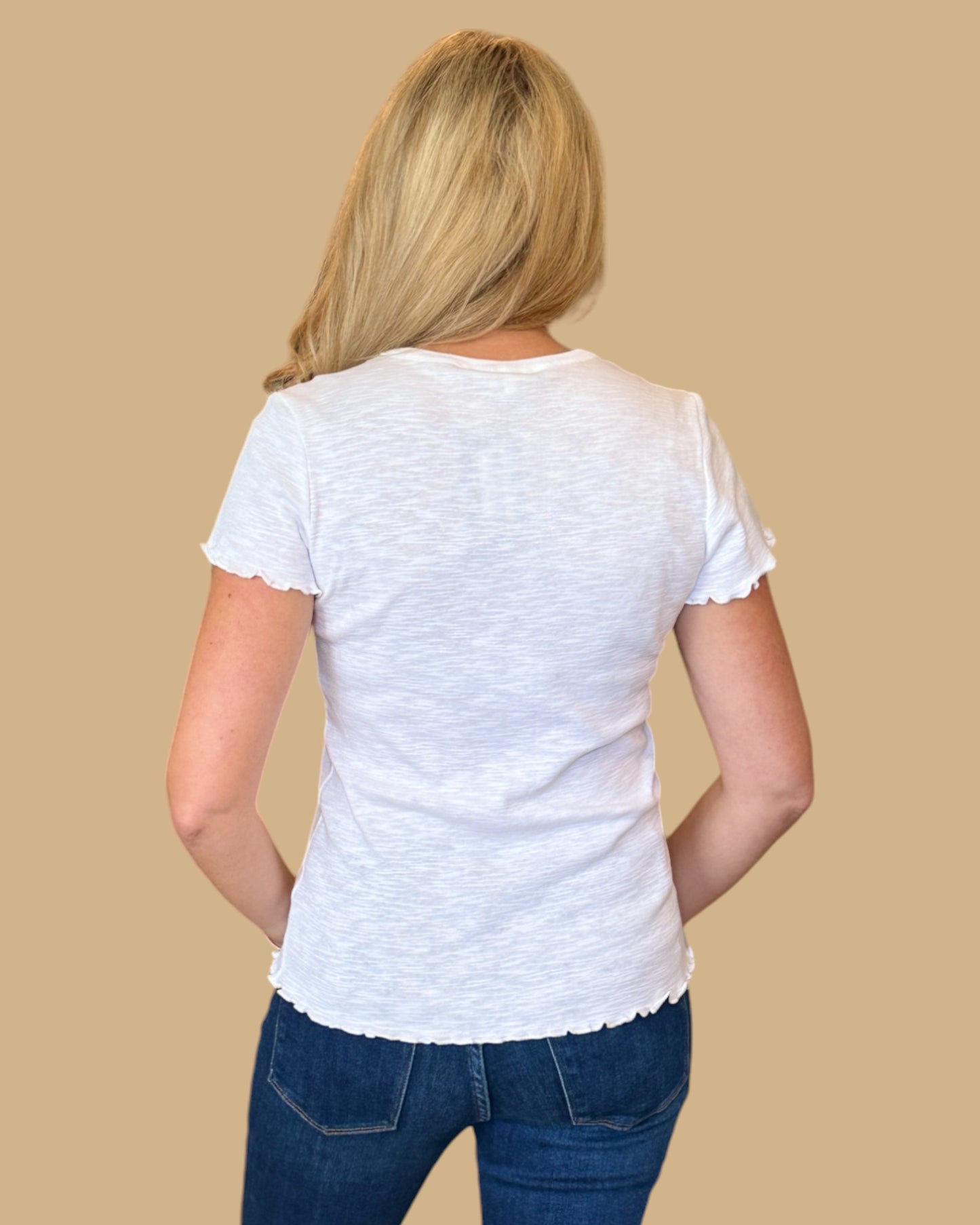 Woman wearing a white short-sleeve tee with ruffled edges, paired with dark wash skinny jeans. Casual, fitted white t-shirt for women, perfect for everyday wear. Available at Wish Upon Boutique.