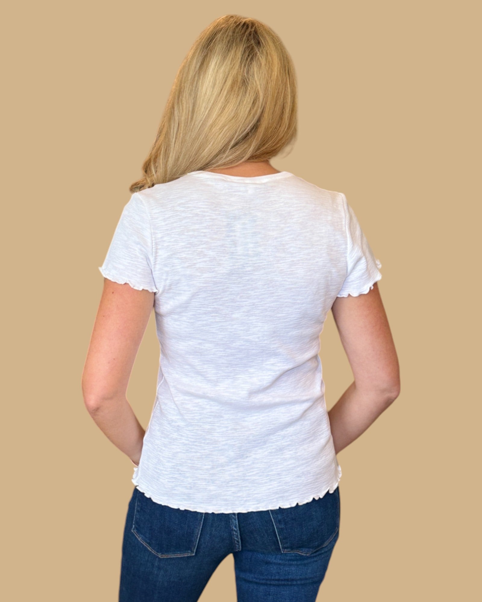 Woman wearing a white short-sleeve tee with ruffled edges, paired with dark wash skinny jeans. Casual, fitted white t-shirt for women, perfect for everyday wear. Available at Wish Upon Boutique.