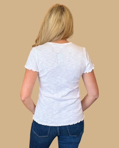 Woman wearing a white short-sleeve tee with ruffled edges, paired with dark wash skinny jeans. Casual, fitted white t-shirt for women, perfect for everyday wear. Available at Wish Upon Boutique.