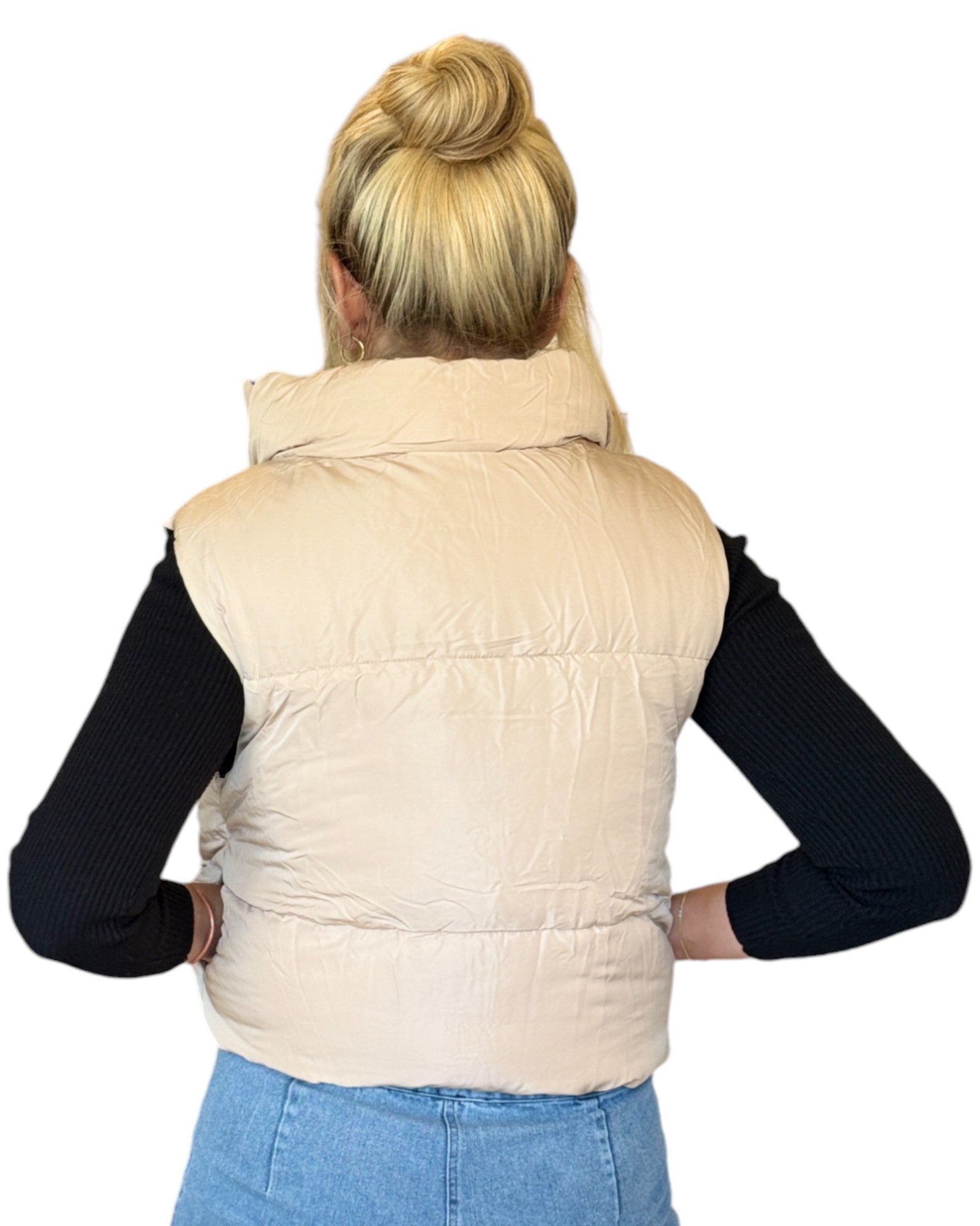 Woman wearing a beige and black reversible puffer vest with a zip-down front and funnel neck, paired with a black top and blue jeans.
