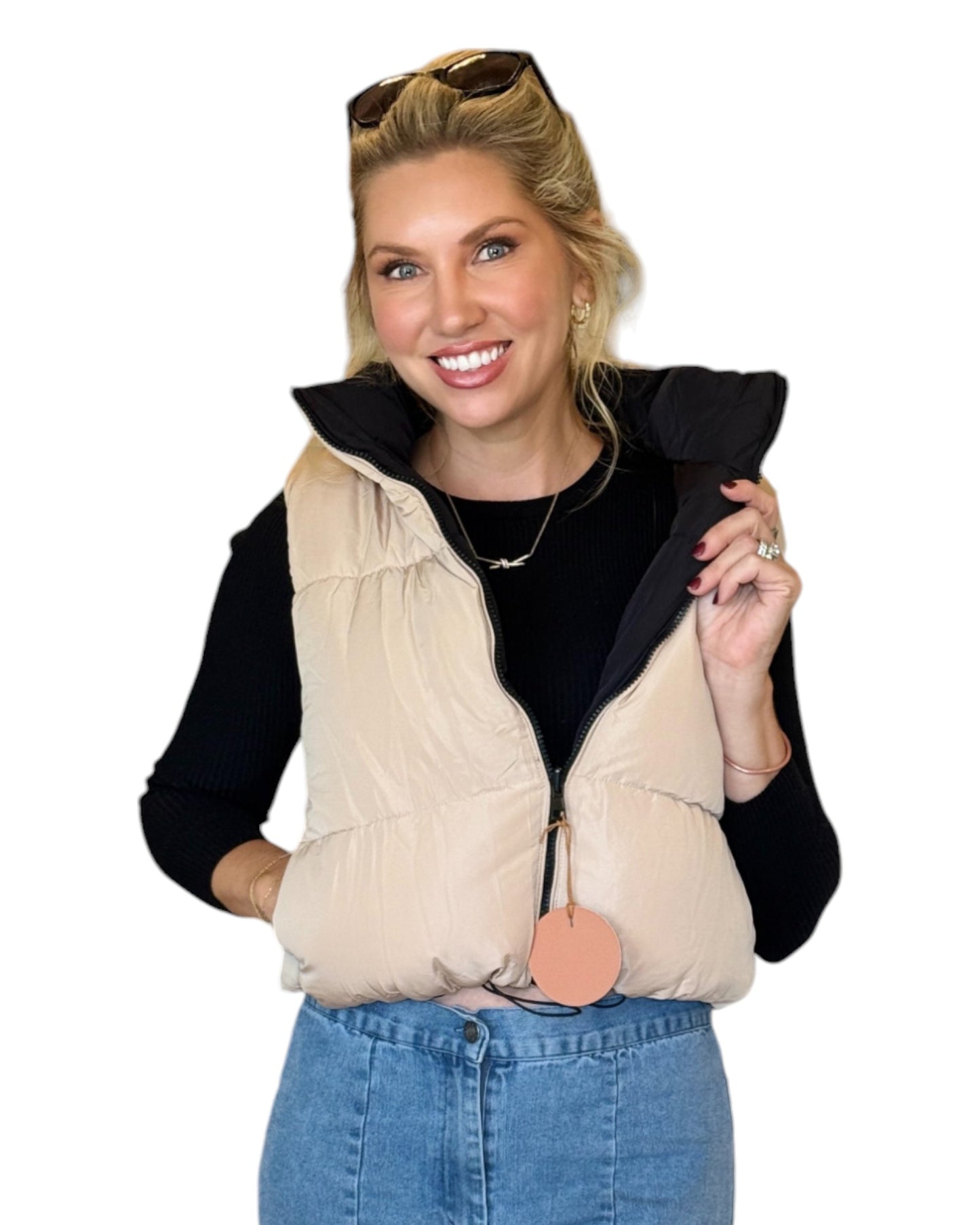 Woman wearing a beige and black reversible puffer vest with a zip-down front and funnel neck, paired with a black top and blue jeans.