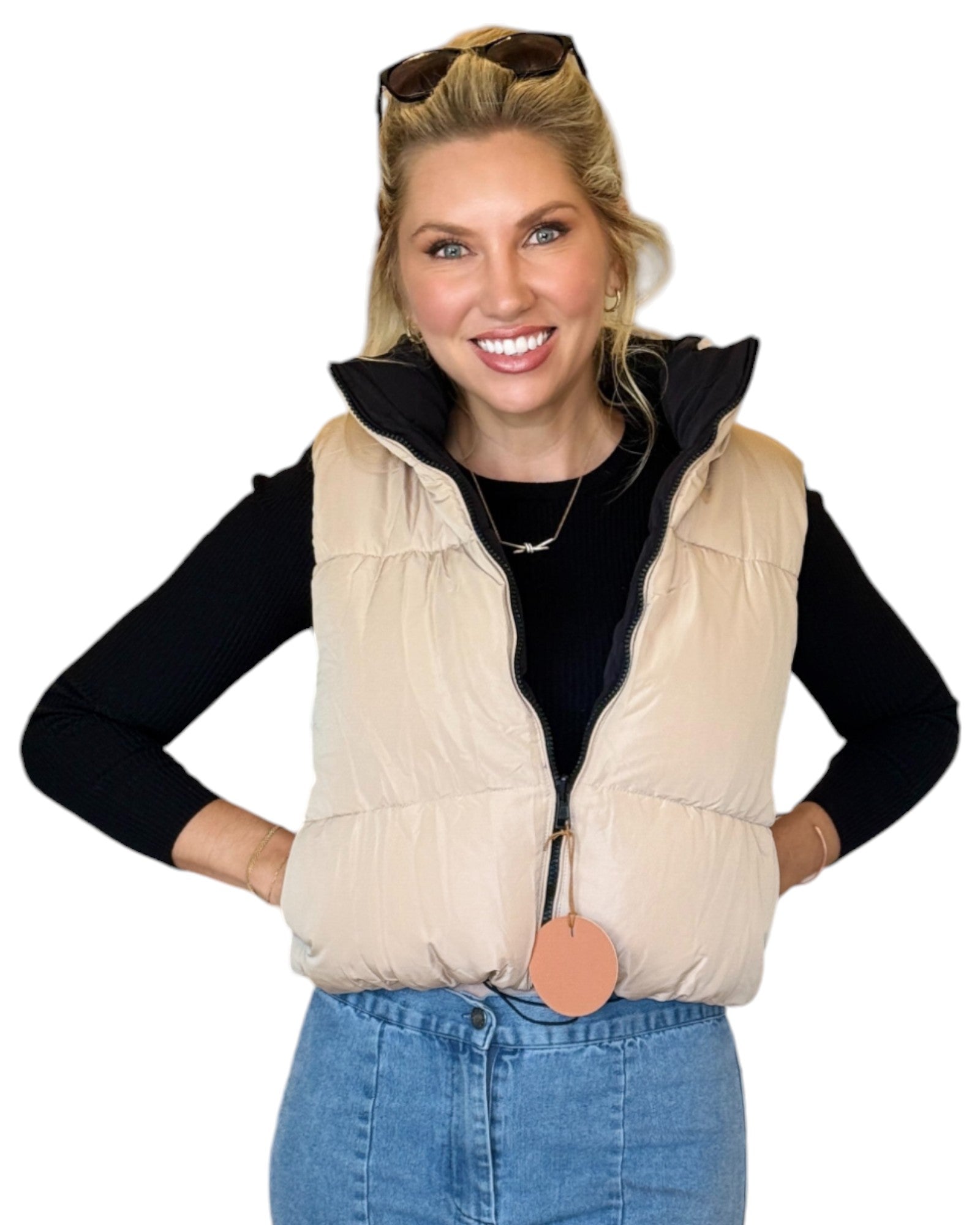 Woman wearing a beige and black reversible puffer vest with a zip-down front and funnel neck, paired with a black top and blue jeans.