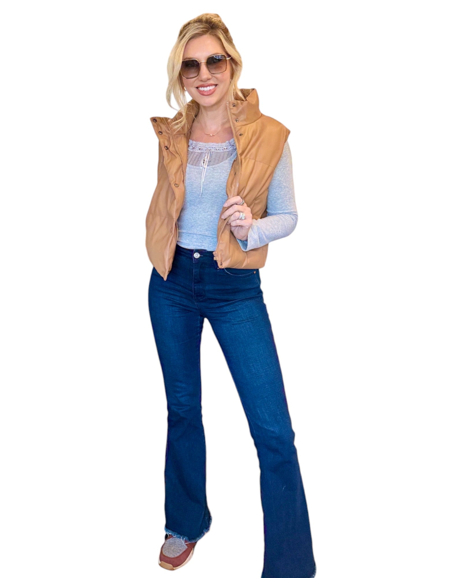 Woman wearing grey soft ribbed long sleeve top with lace tie accent, dark blue jeans and faux leather tan puffer vest. 