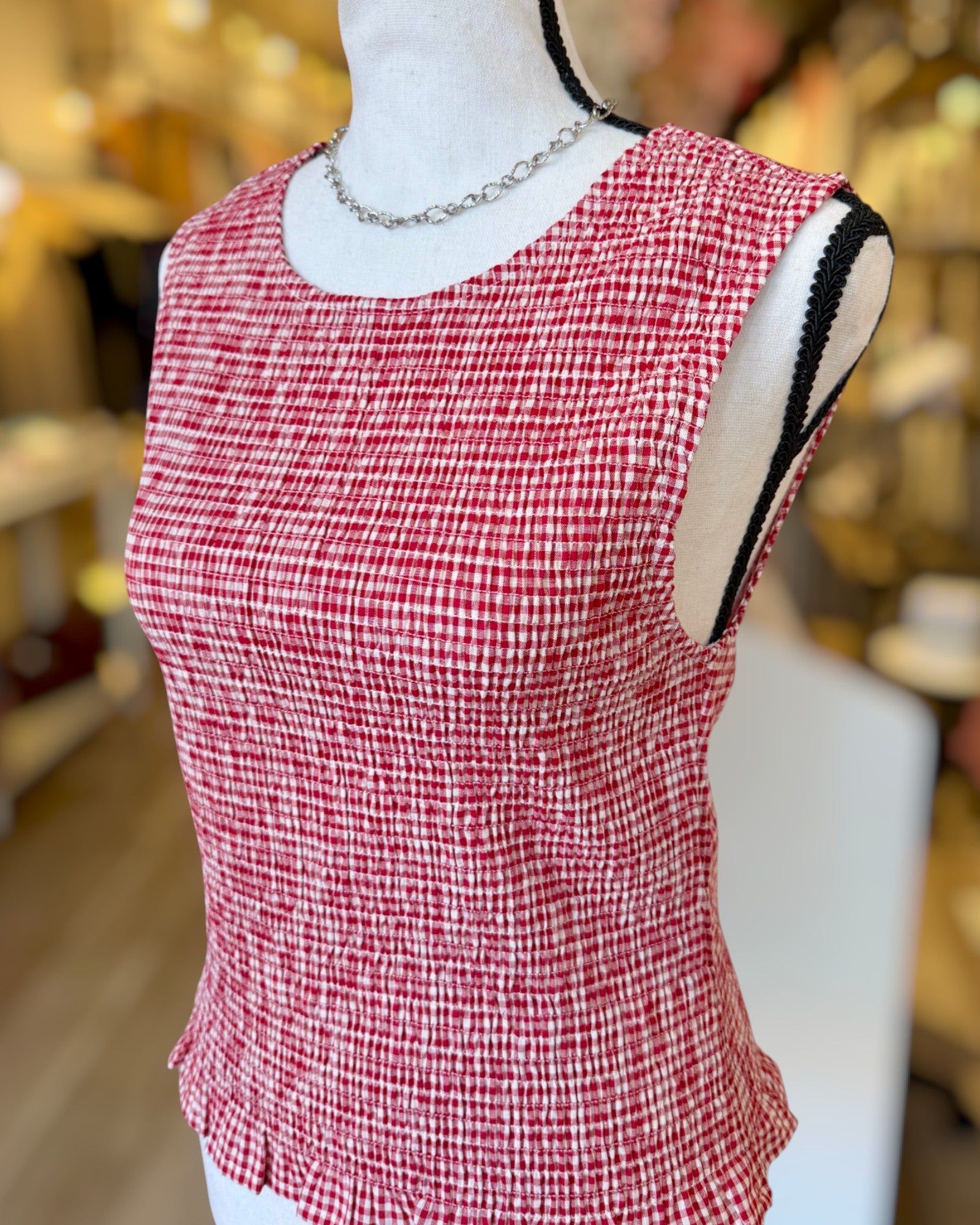 Red and white checkered sleeveless top on a mannequin with a blurred background.