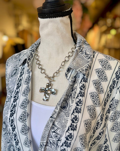 Mannequin wearing a patterned collared top with a necklace featuring a cross pendant.