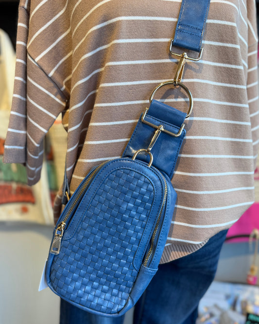 Vegan leather blue crossbody bag with gold hardware against a tan stripe shirt.