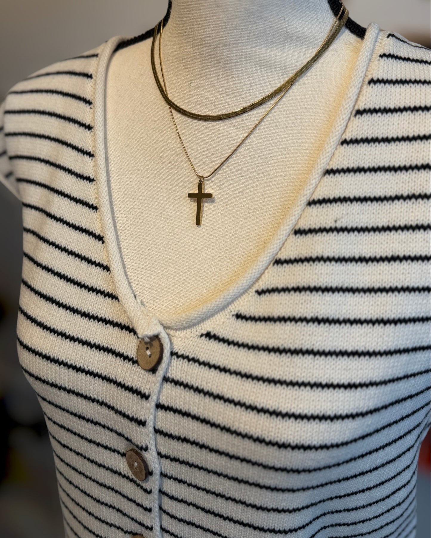 Mannequin wearing a striped shirt with a necklace featuring a cross pendant.