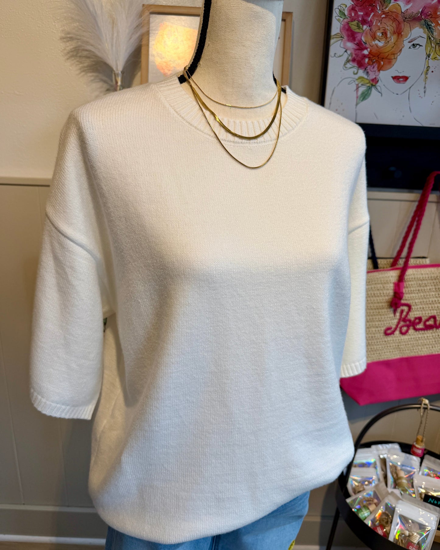Mannequin wearing a white sweater with a gold necklace in a casual setting.