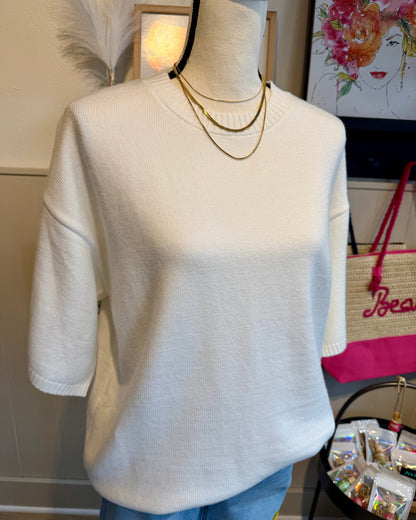 Mannequin wearing a white sweater with a gold necklace in a casual setting.
