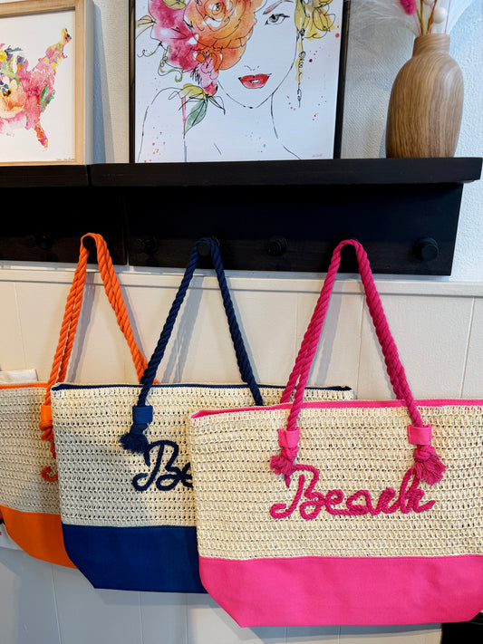 3 straw beach bags in orange, navy and pink with the word "beach".