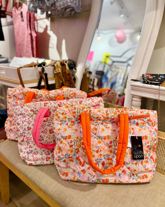 Floral-patterned bags with orange and pink handles on a store bench.