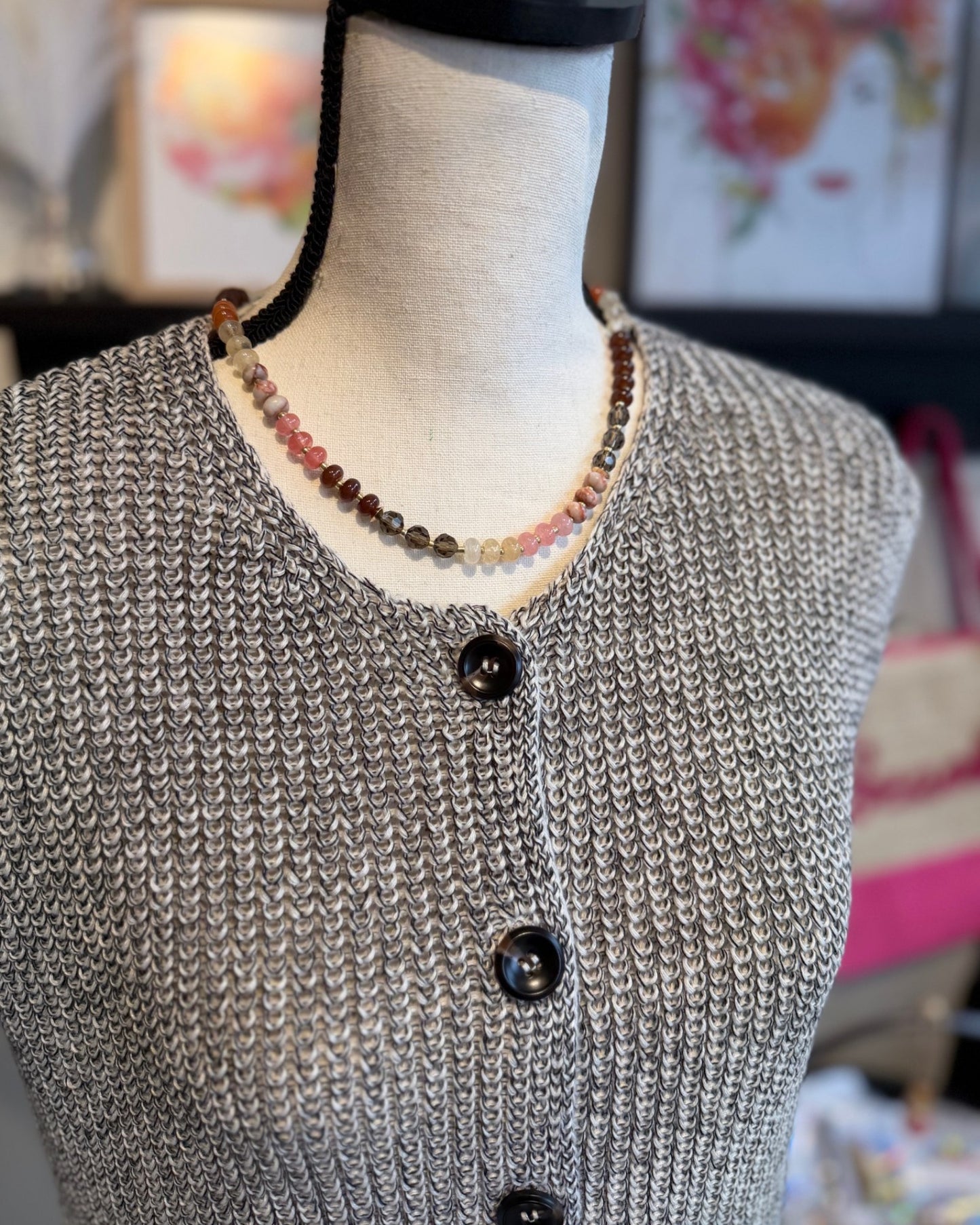 Mannequin wearing a gray knitted vest with dark brown buttons, set against a blurred indoor background.
