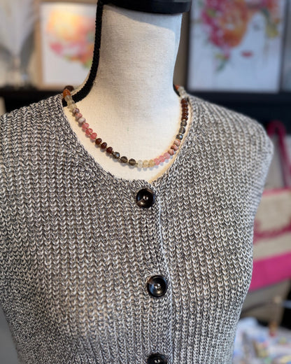 Mannequin wearing a gray knitted vest with dark brown buttons, set against a blurred indoor background.