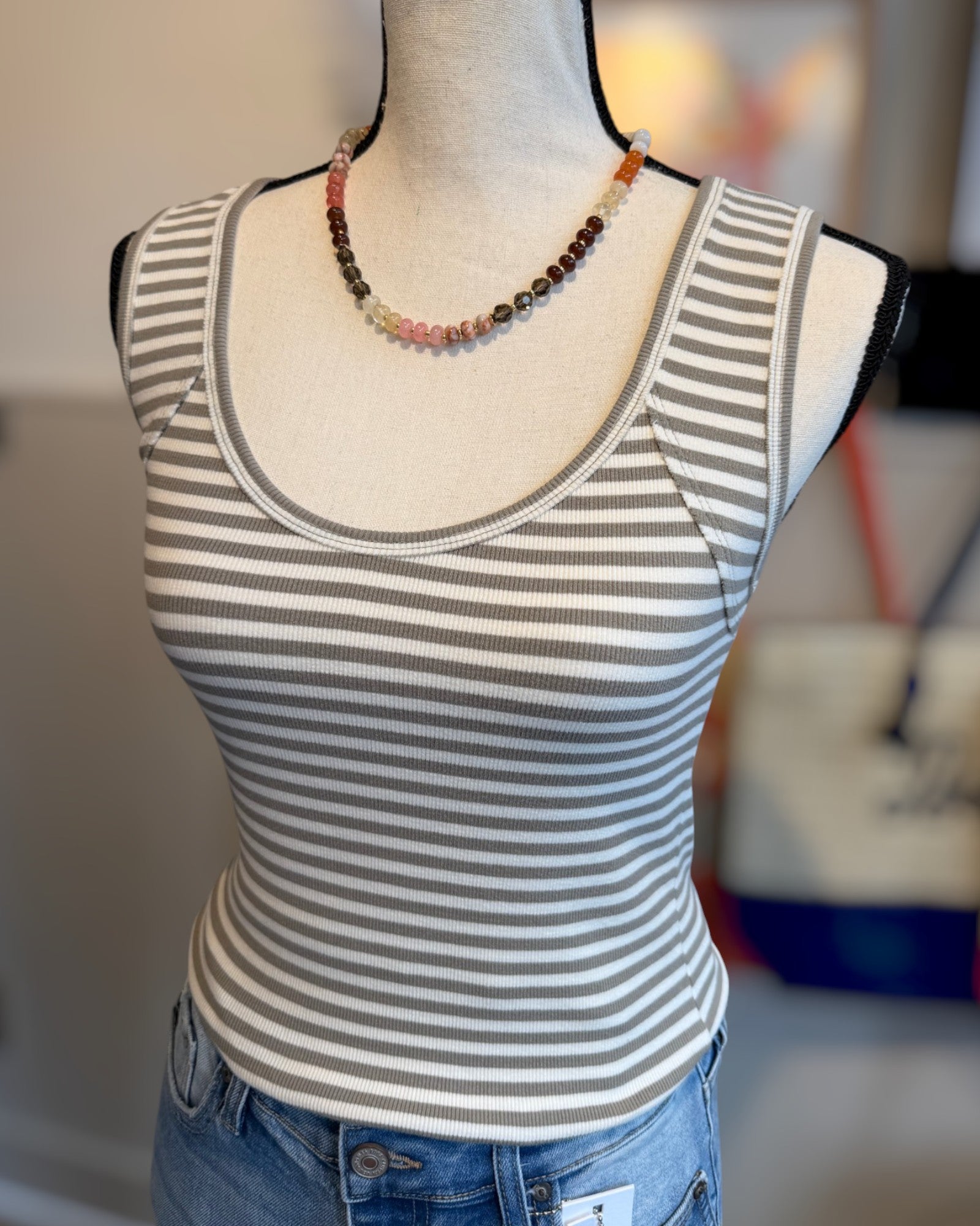 Mannequin wearing a striped tank top and jeans with a blurred background.