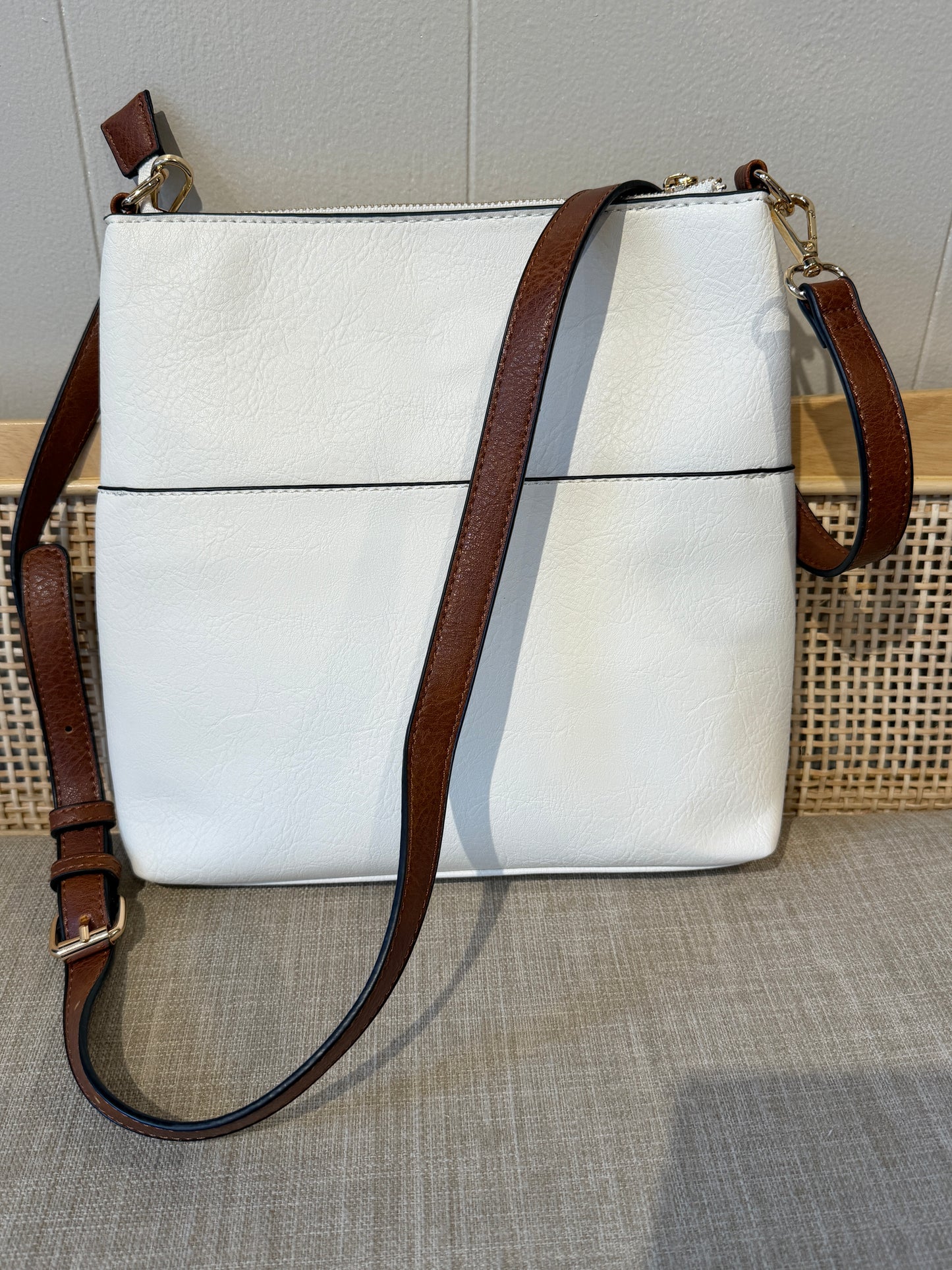 A white pebbled leather crossbody bag with a brown leather strap and gold-tone hardware, displayed on a textured beige surface.