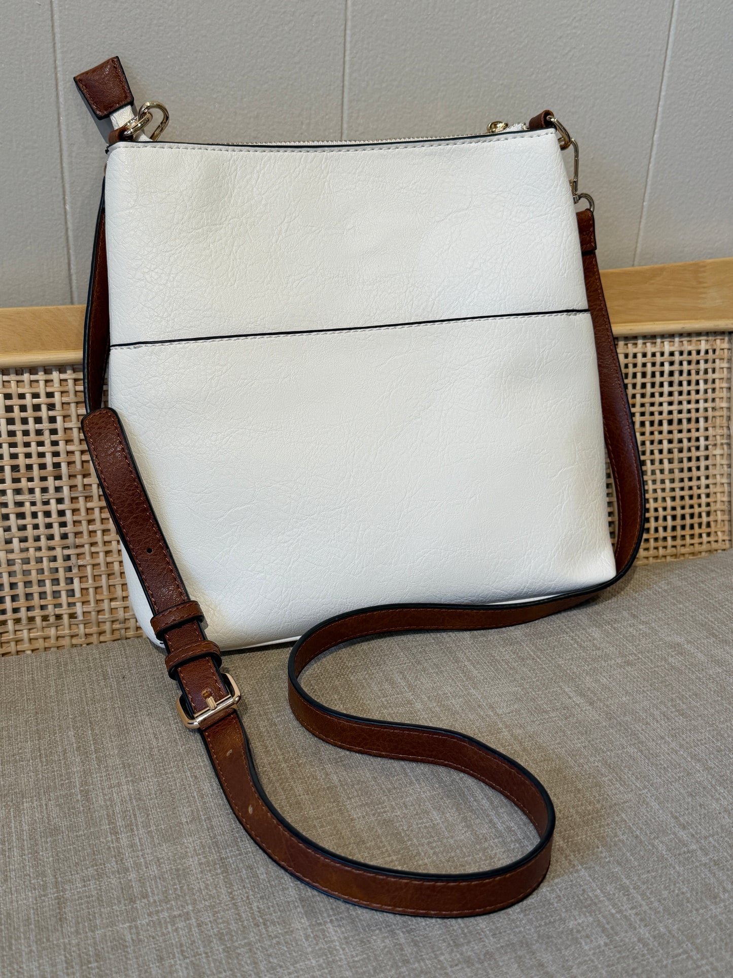 A white leather shoulder bag with a brown leather strap and trim, displayed on a textured beige surface against a neutral background.