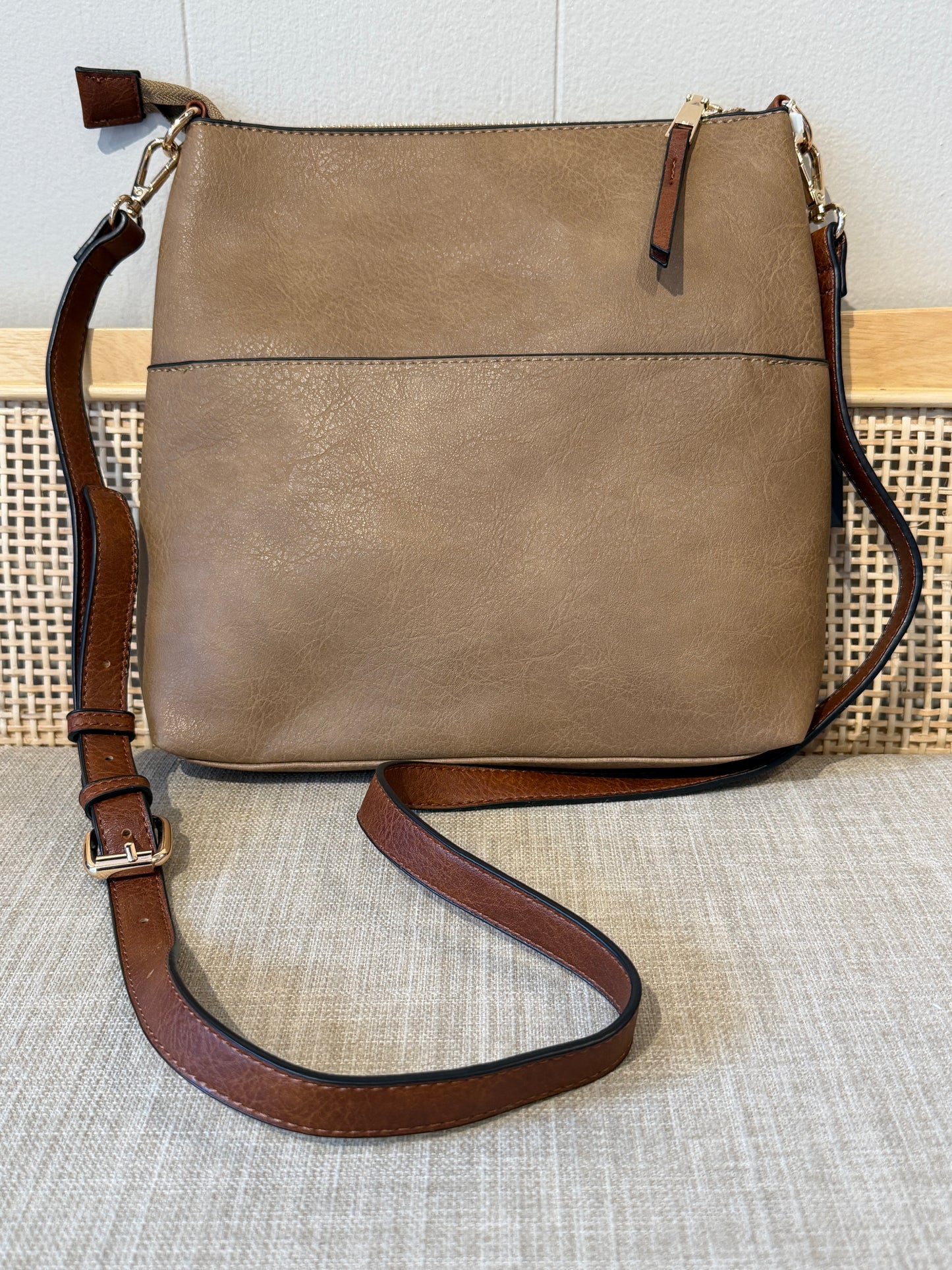 A mocha faux-leather crossbody bag with a brown leather strap and gold-tone hardware, displayed on a textured beige fabric surface.