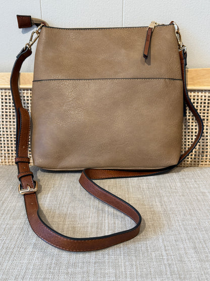 A mocha faux-leather crossbody bag with a brown leather strap and gold-tone hardware, displayed on a textured beige fabric surface.