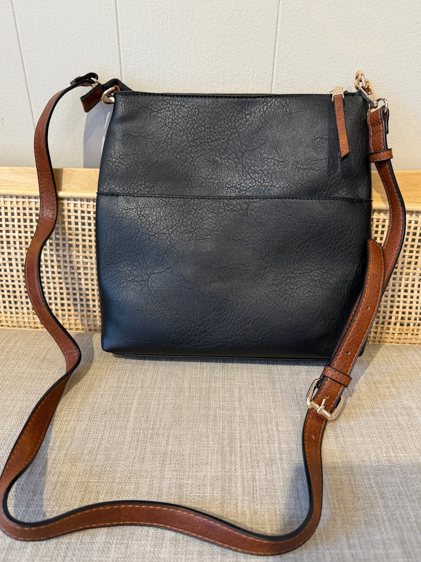 Black faux-leather crossbody bag with a brown leather strap and gold-tone hardware, displayed against a neutral background.