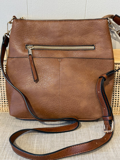 A brown faux-leather crossbody handbag with a back zippered pocket, shown on a textured beige surface against a light wall.