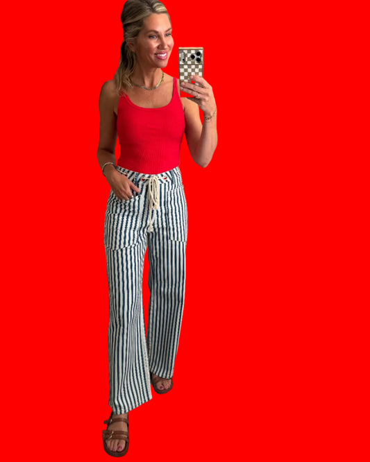 A woman taking selfie showing off a red tank top and blue-and-white vertically striped wide-leg pants. 