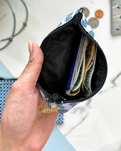 Hand holding a small pouch with black interior containing money and cards against a blurred background.