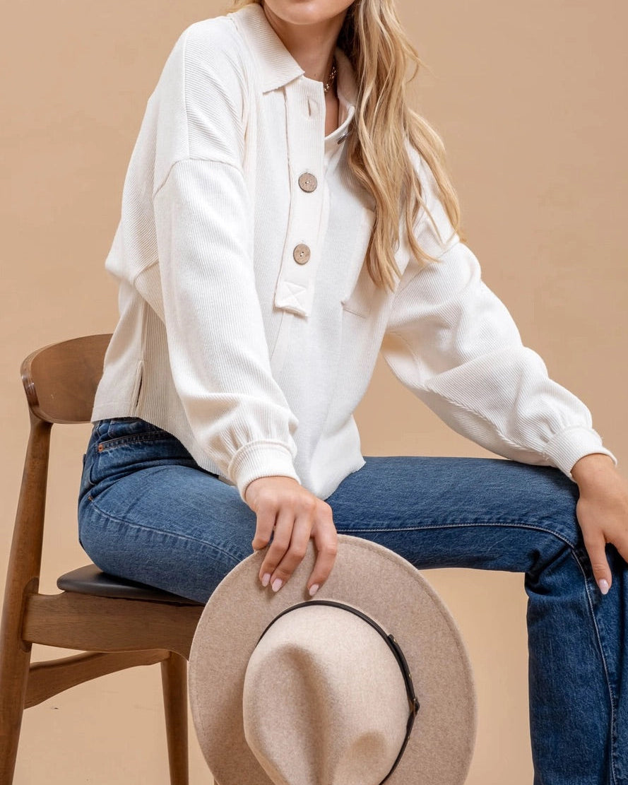 Woman wearing an ivory casual top with oversized buttons and blue jeans on a beige background.