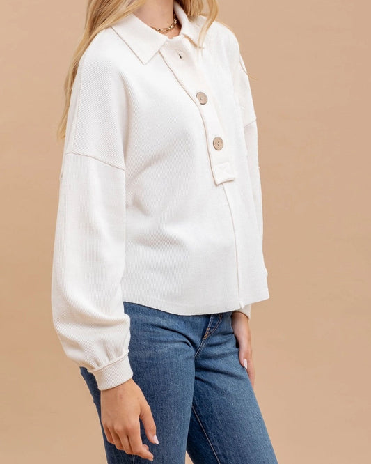 Woman wearing an ivory casual top with oversized buttons and blue jeans on a beige background.