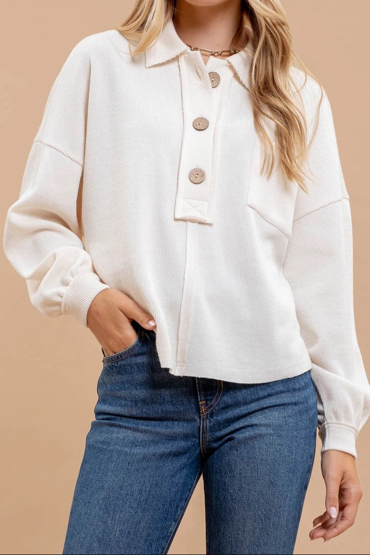 Woman wearing an ivory casual top with oversized buttons and blue jeans on a beige background.