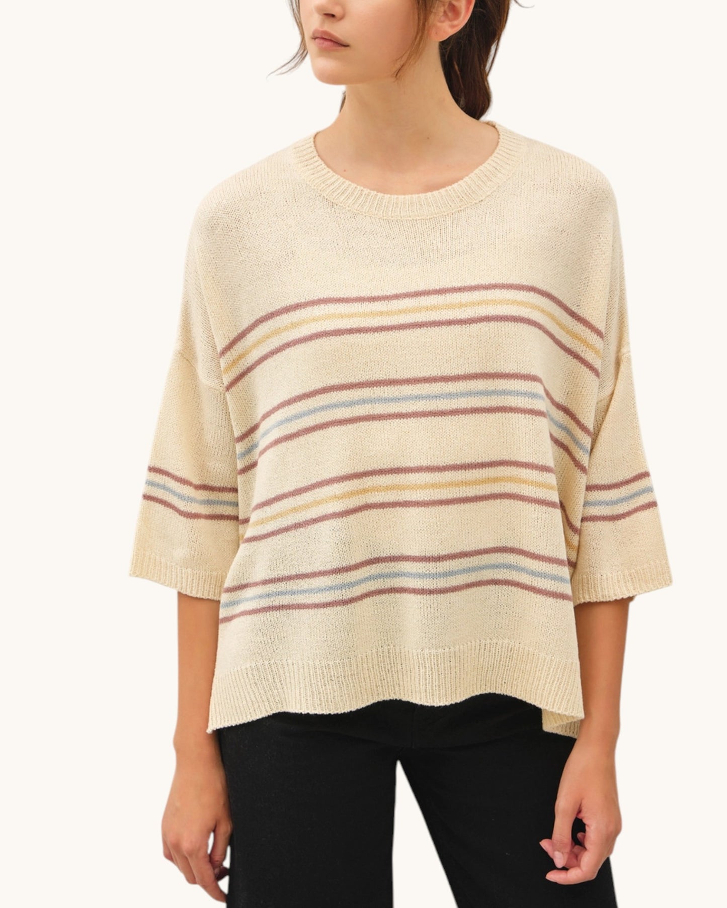 Woman wearing a cream-colored sweater with multicolor stripes on a white background.