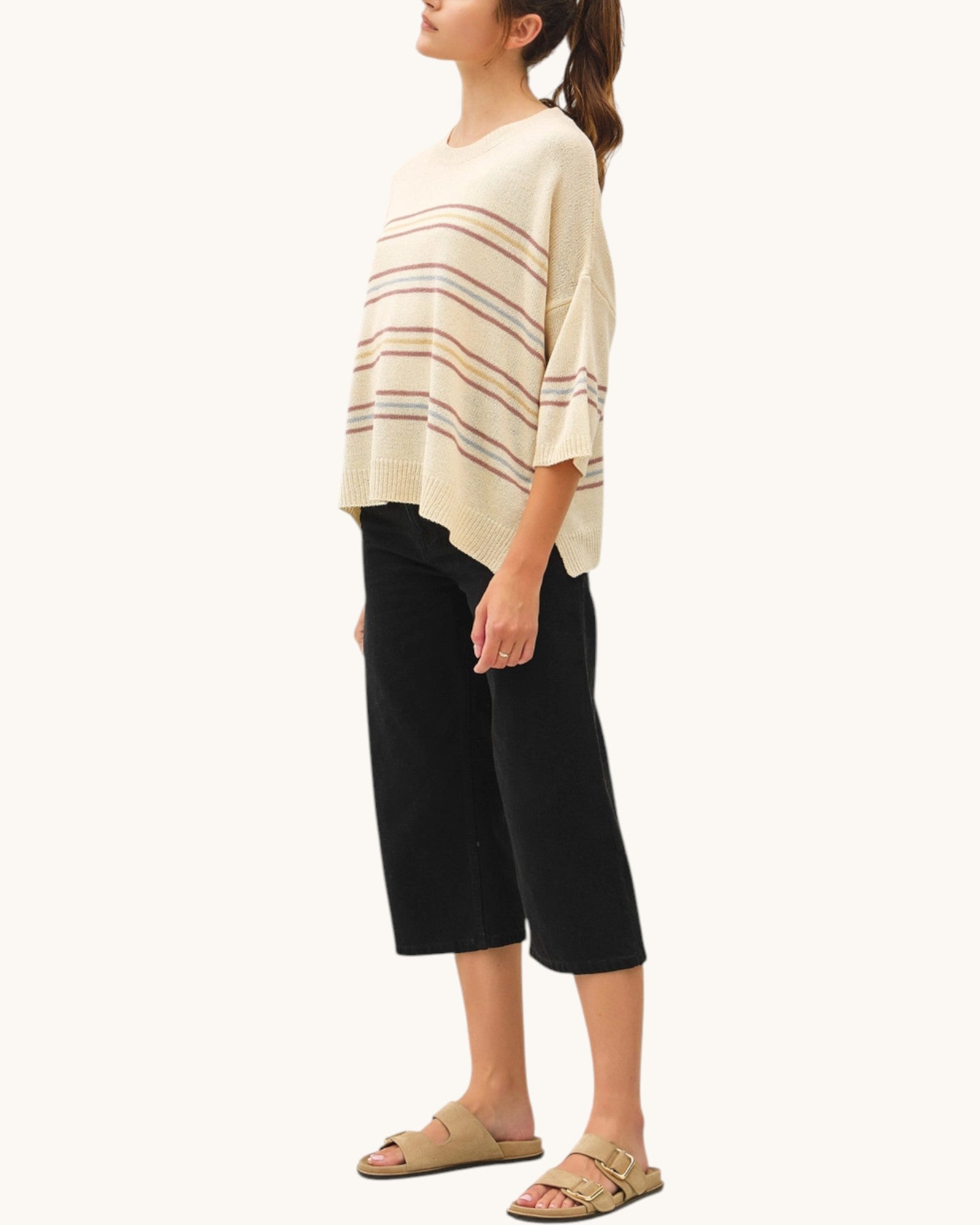 Woman wearing a light beige striped sweater and black pants on a white background.