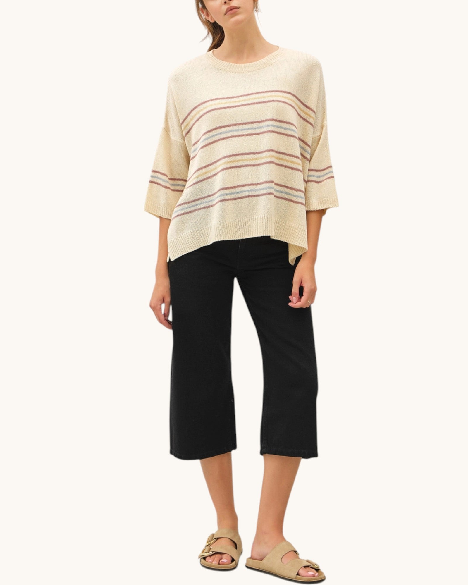 Woman wearing a light beige striped sweater and black pants on a white background.