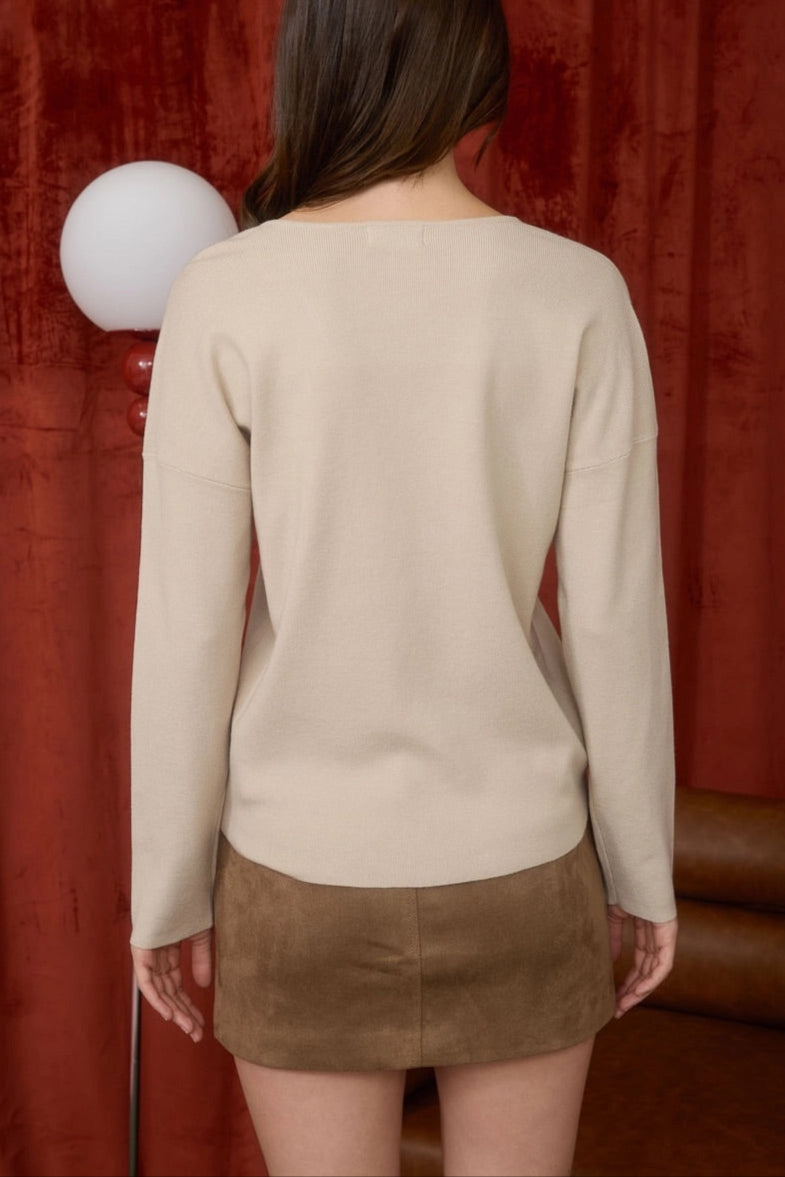 Woman wearing a beige sweater and brown skirt against a rust curtain background.