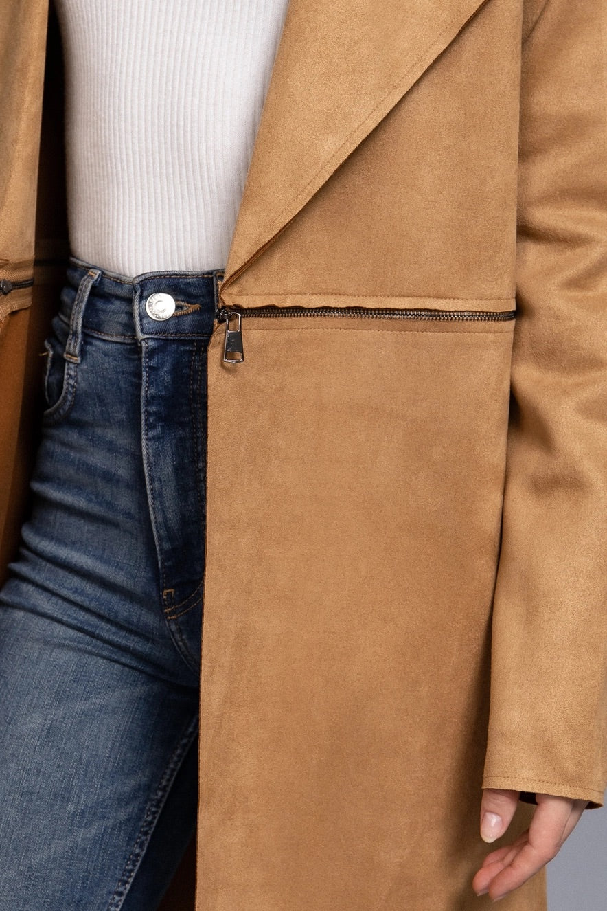 Person wearing a tan suede coat over a white shirt and blue jeans.