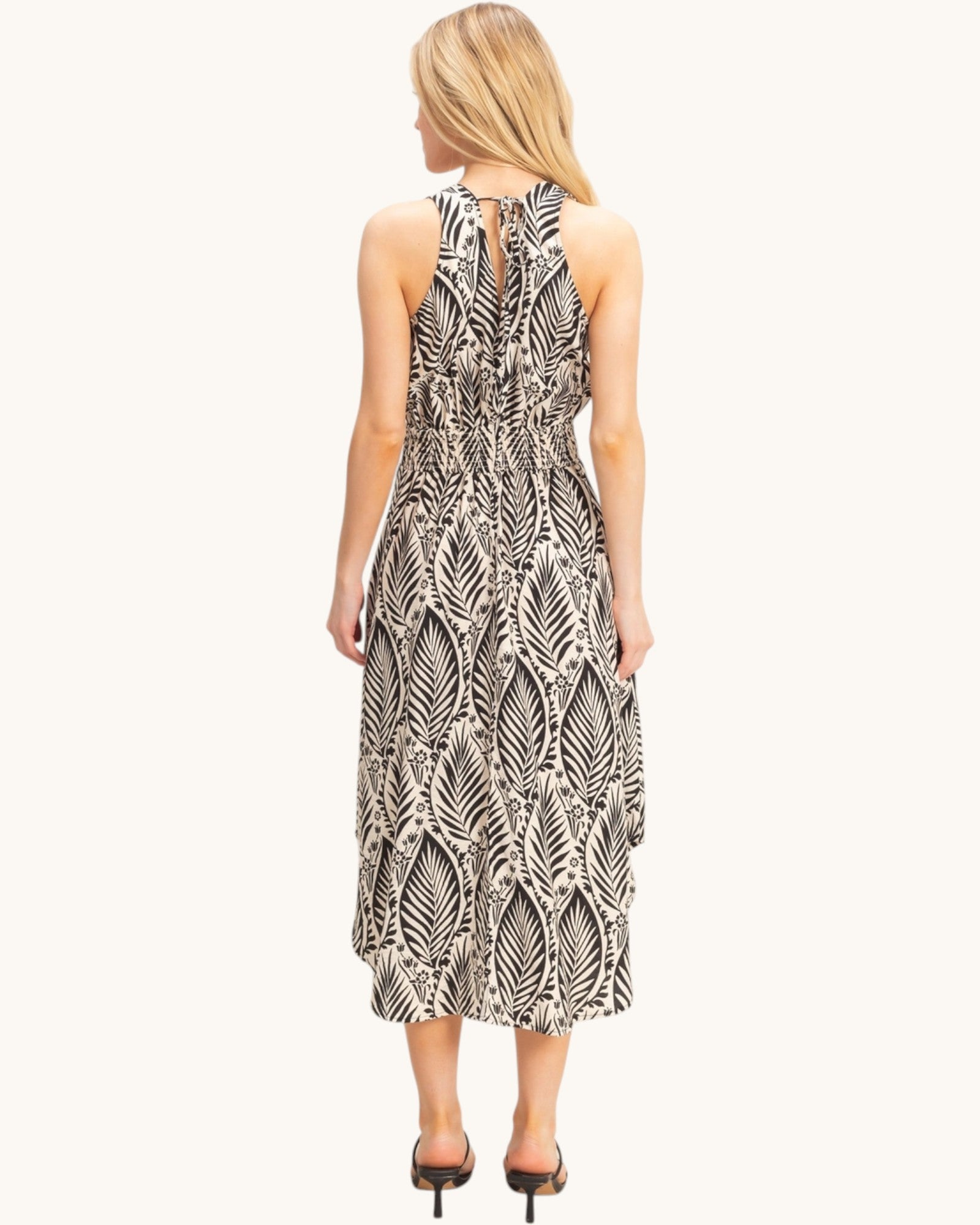 Back view of a woman wearing a tropical patterned beige dress on a white background.