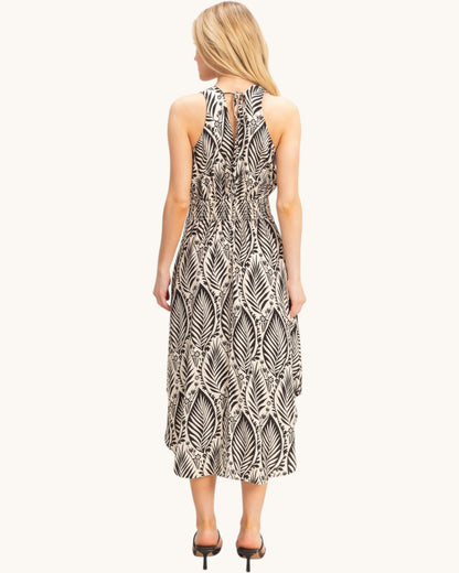 Back view of a woman wearing a tropical patterned beige dress on a white background.