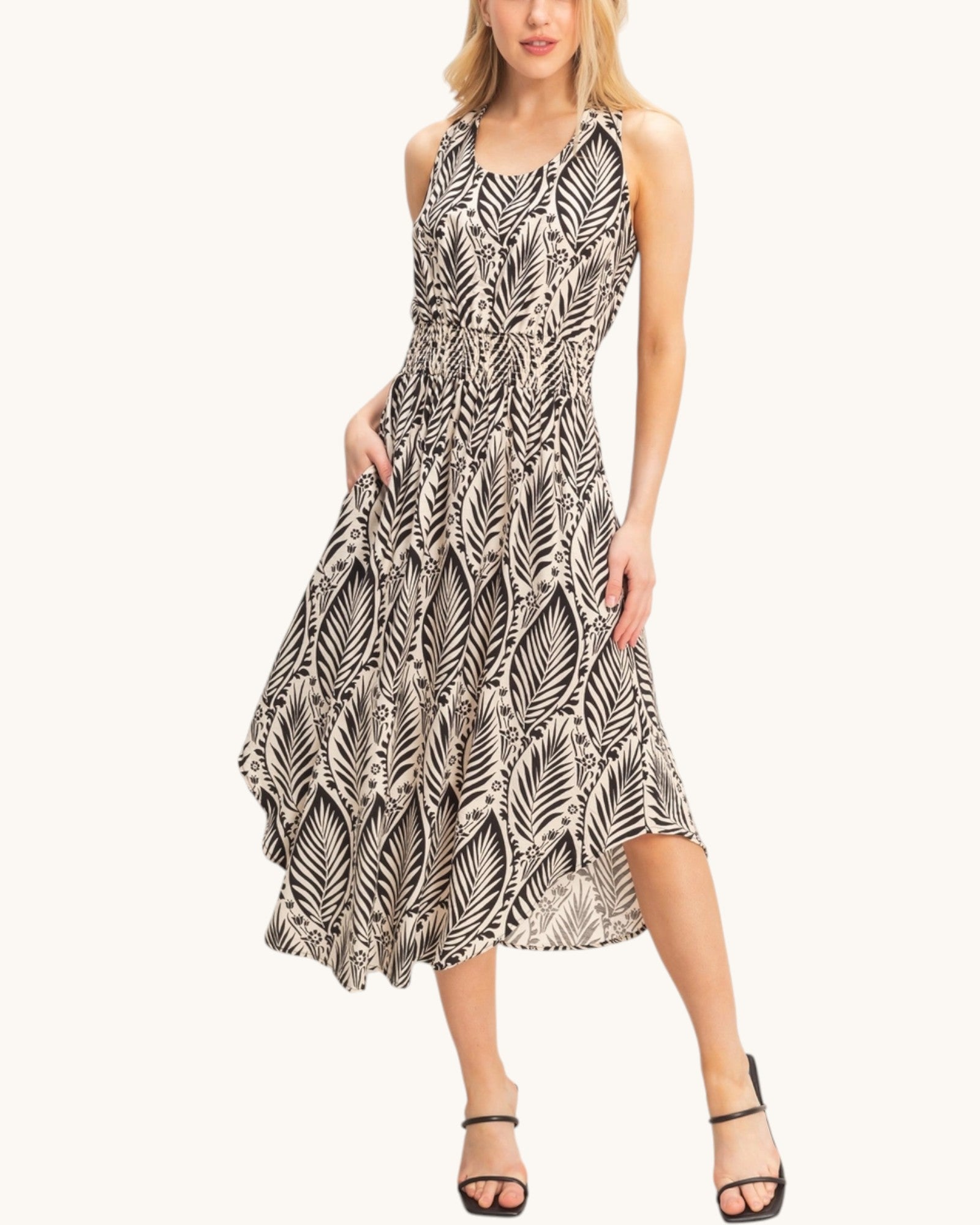 Woman wearing a beige sleeveless dress with a black leaf pattern on a white background.