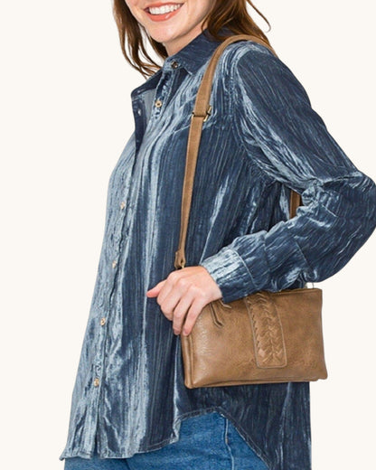 Woman wearing a blue  shirt holding a brown leather handbag on a white background.