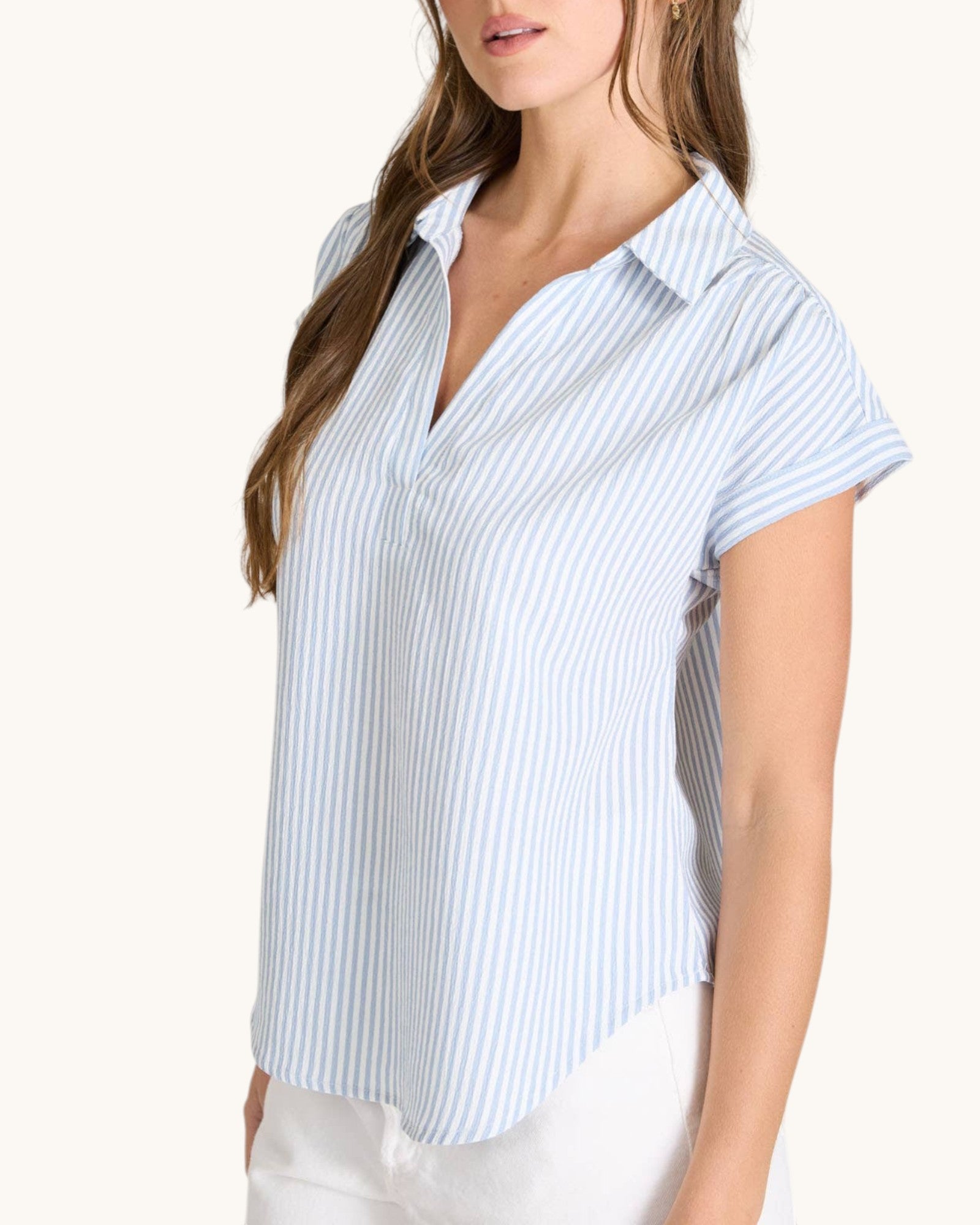 Woman wearing a short-sleeve, blue and white striped shirt on a white background.