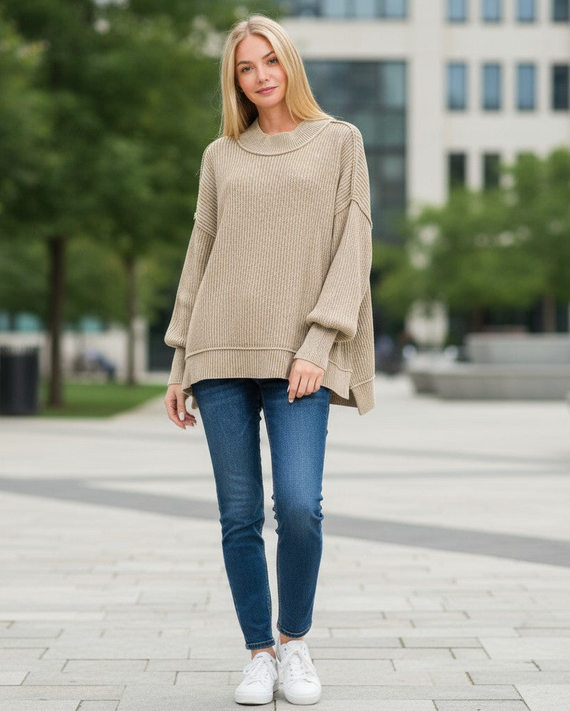 Woman wearing a light mocha sweater and blue jeans standing in an urban setting. 
