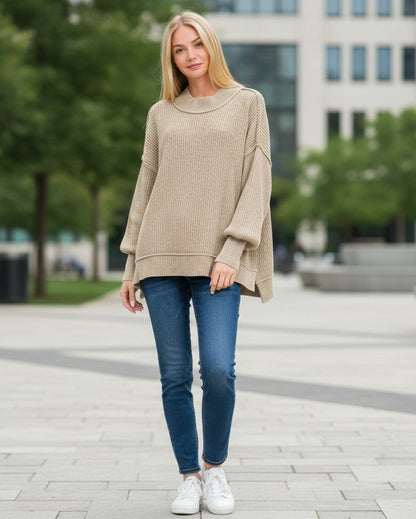 Woman wearing a light mocha sweater and blue jeans standing in an urban setting. 