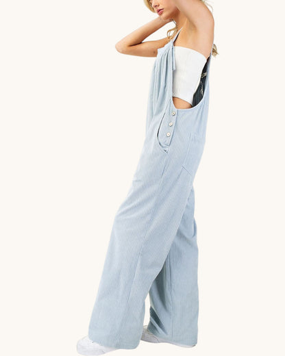 A woman wearing light blue wide-leg corduroy overalls with a white strapless top, shown from the side against a plain off-white background.
