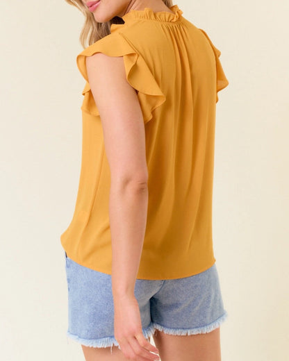 Woman wearing a yellow ruffled top and denim shorts against a plain background.