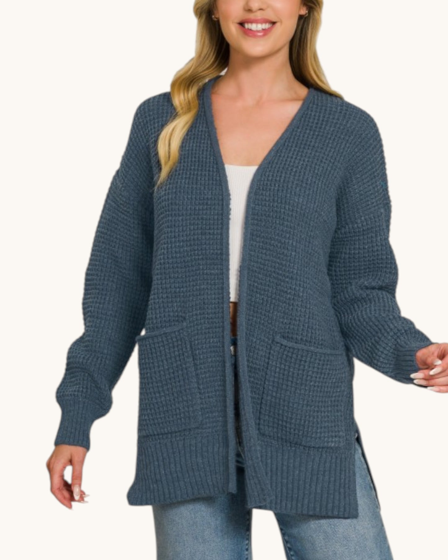 Woman wearing a Navy waffle knit open cardigan with blue jeans and a white cropped tank top. 