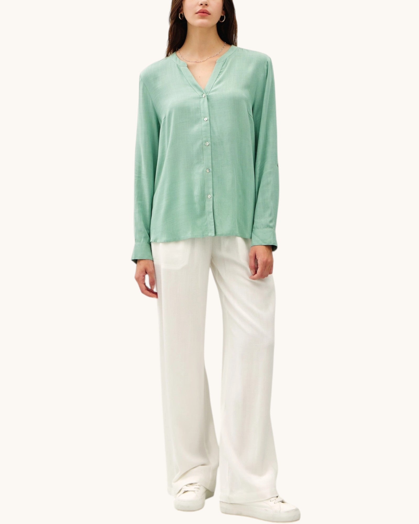 Person wearing a light green long-sleeve top and white pants on a white background.