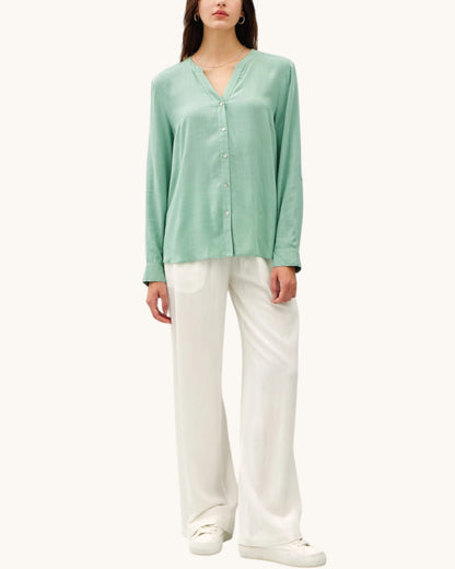 Person wearing a light green long-sleeve top and white pants on a white background.